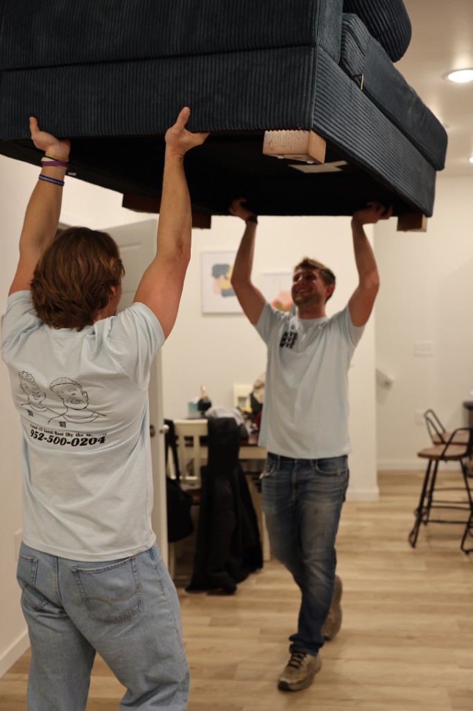 Two Move Move Move movers carrying a sectional sofa through a home